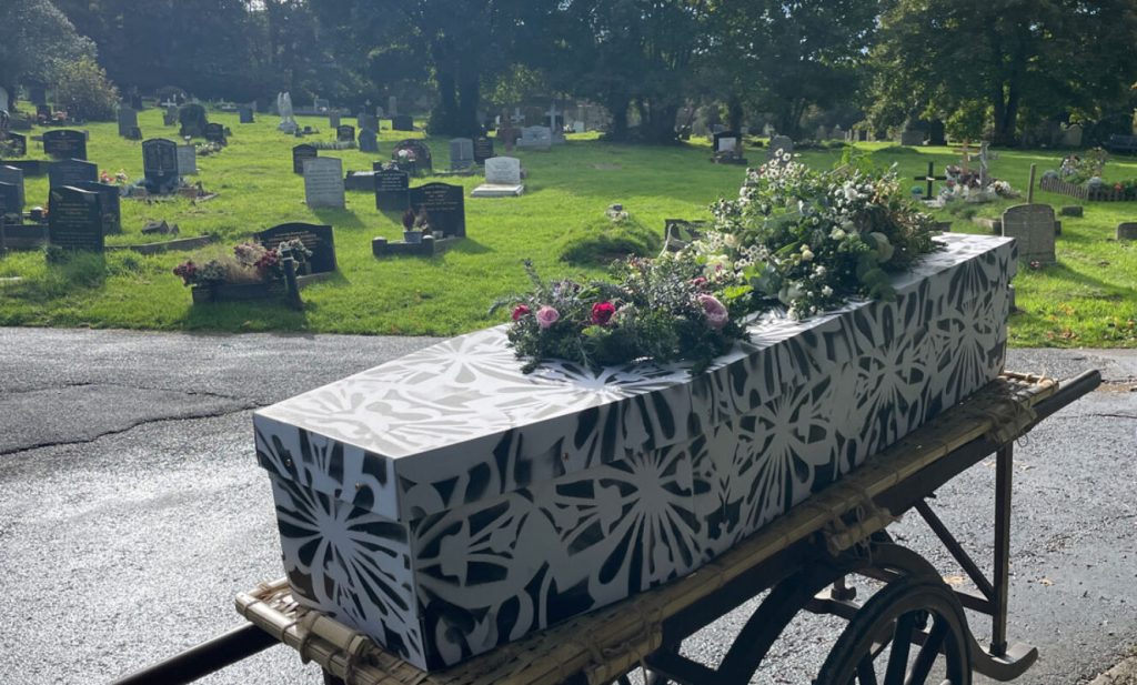 Decorative cardboard coffin with hand-printed pattern on funeral trolley