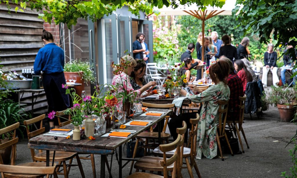 People gathered around long tables outdoors for a memorial lunch in a garden setting
