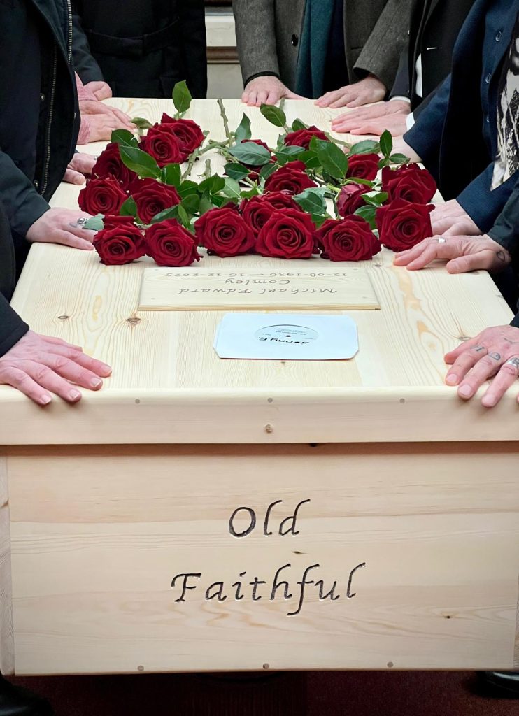 Guests placing hands on Feet First hand crafted coffin with personalised name, 'Old Faithful'