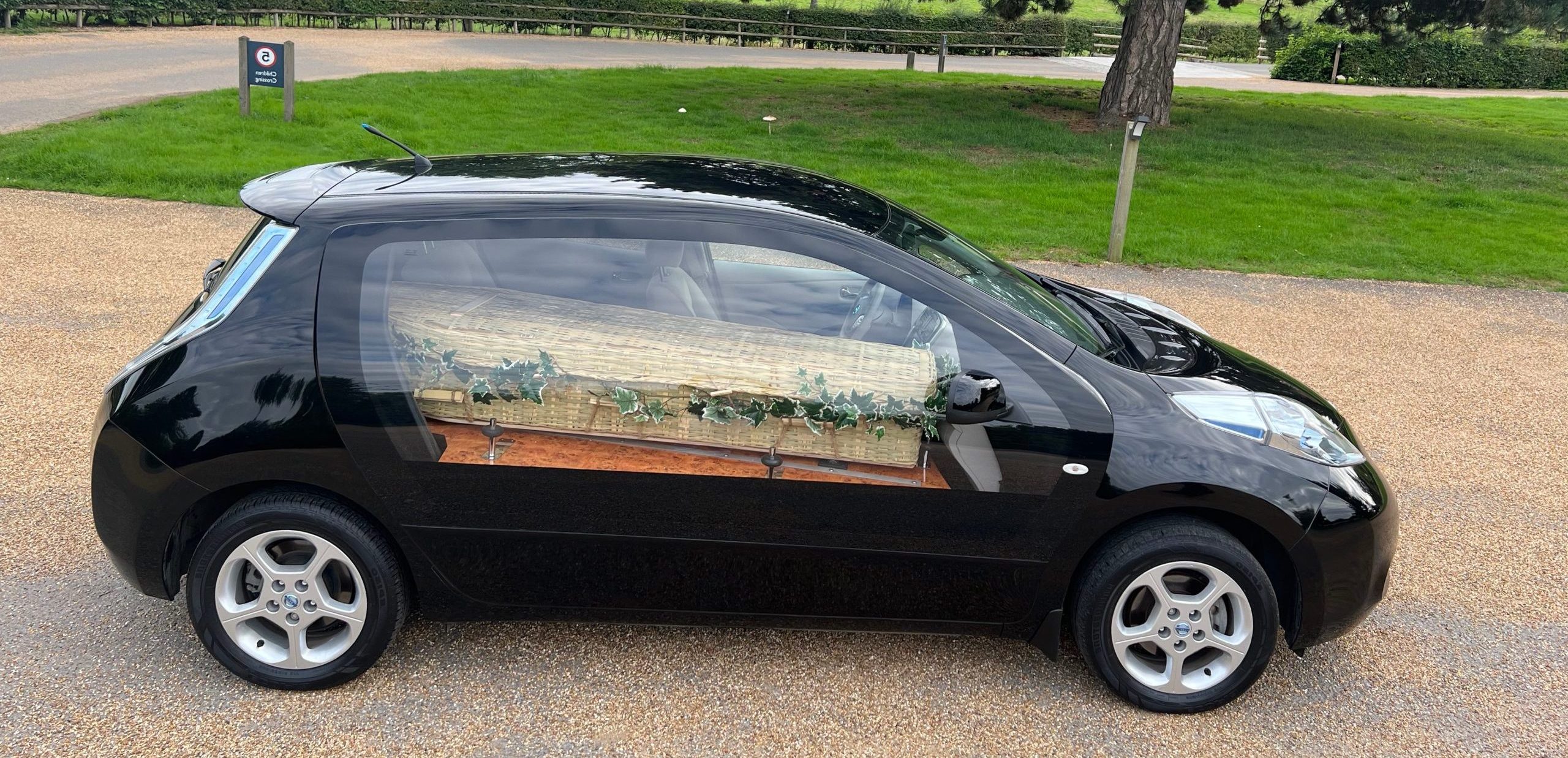 Black electric hearse side view with wicker coffin inside