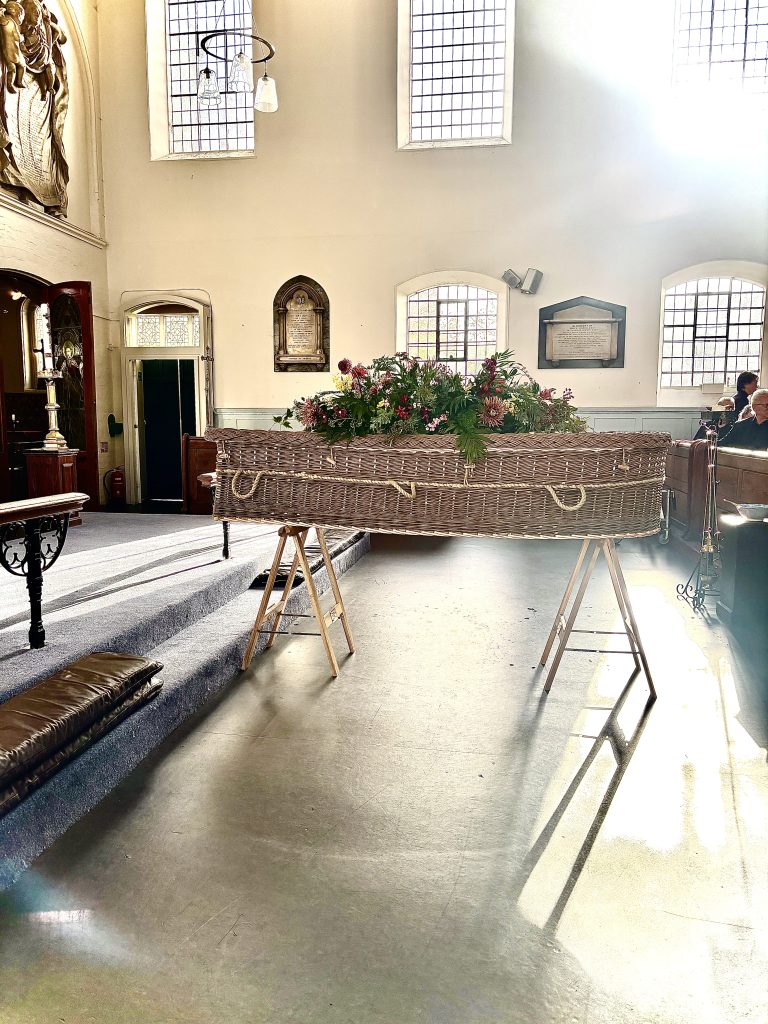 Brown willow petal shaped coffin in situ at the church dressed with flowers